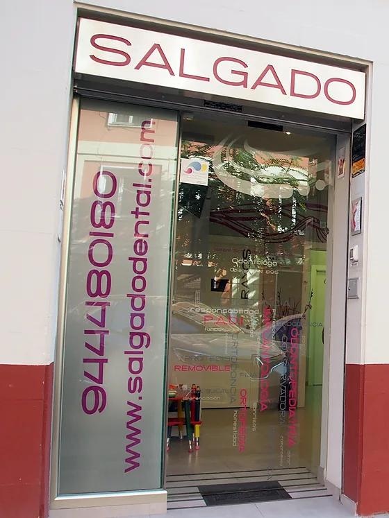 La entrada de Salgado Dental en la calle Arturo Campión: rótulo en letras granates sobre fachada blanca y zócalo rojo.